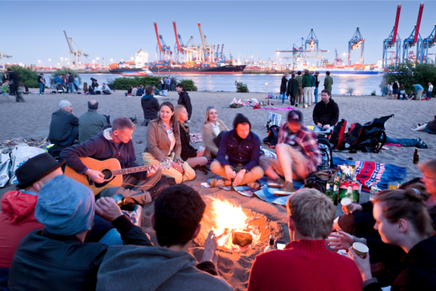 Der Elbstrand lockt auch in den Abendstunden viele Menschen an, um vor der eindrucksvollen Hafenkulisse ihre Freizeit zu verbringen – hier mit Lagerfeuer und Musik.